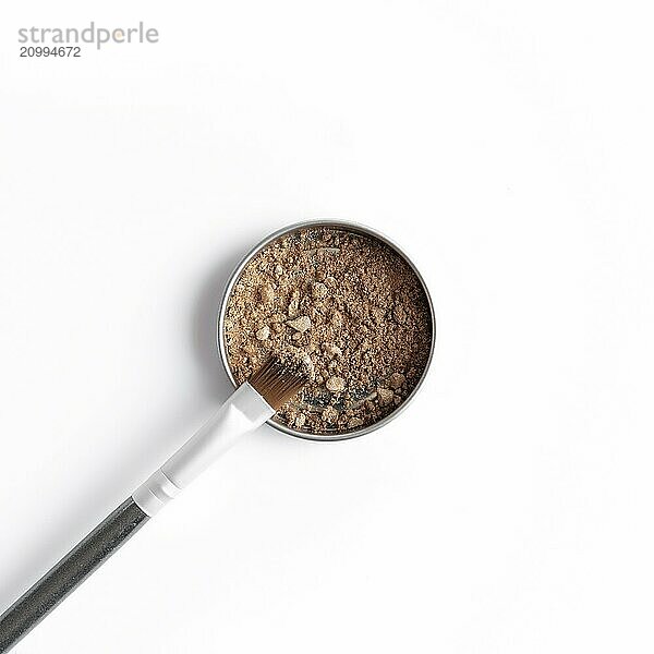 Light brown face shadow in container and eye shadow or make-up brush. Makeup concept flat lay on white background