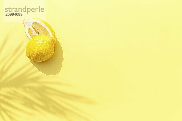 Two halved cuts of lemon with shadow from palm leaf on yellow background. Healthy eating  travel or vacation concept