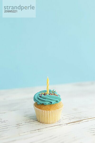 Birthday greetings concept. Yellow candle on a muffin or cupcake. Blue background. Wooden table