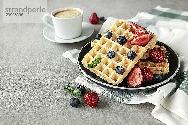 Sweet delicious breakfast with plate of waffles  strawberry and blueberry  mint leaf and cup of coffee on concrete gray background.