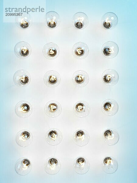 Array of lit incandescent tungsten light bulbs on blue background