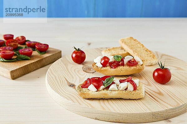 Italian crostini with mozzarella  cherry tomatoes and basil over a cutting board and blue background