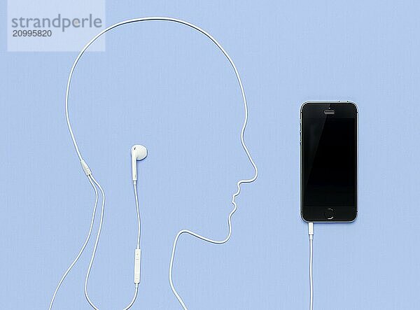 Man head outline made by a headphone cord plugged into iPhone 5s smartphone. Creative music concept on blue background