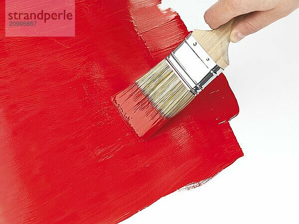 Person holding a paintbrush putting a red coat of paint over white background