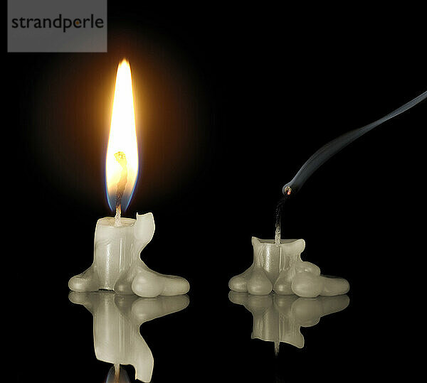 Conceptual stock photo of One short candle is still burning while the other has gone out Abstract concept for economy and energy conservation Isolated silhouettes on black background