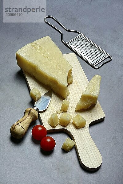 A piece of Parmesan cheese and chopped pieces of cheese on a wooden board