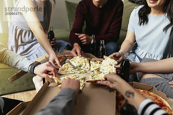 A pizza party  a group of friends chatting and happily eating pizza at the table and drinking sweet soda water. Top view from the second floor.