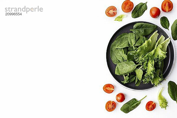 Flat lay with bowl of fresh green salad leaves  lettuce  spinach and red cherry tomatoes cups and halves on a white background. Healthy vegetarian eating concept.