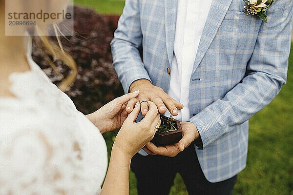 Bride puts wedding ring on groom finger. Boutonniere. Blurred background.