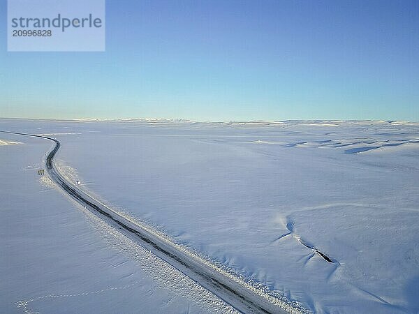 Beautiful aerial drone view landscape. Frozen road in winter in Iceland. Snowy roadsides during winter with blue sky