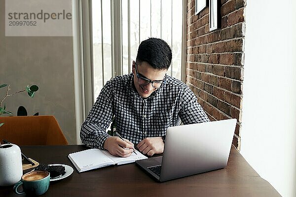 Man working at the laptop with a cup of coffee at home. Blurred background.