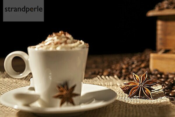 Close-up of coffee cup with whipped cream and star anise on a black background