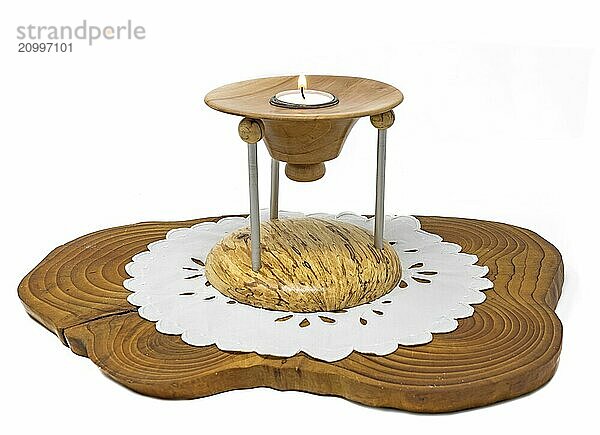 Multi-piece wooden candlestick with a burning candle stands on a dark wooden board on a white background