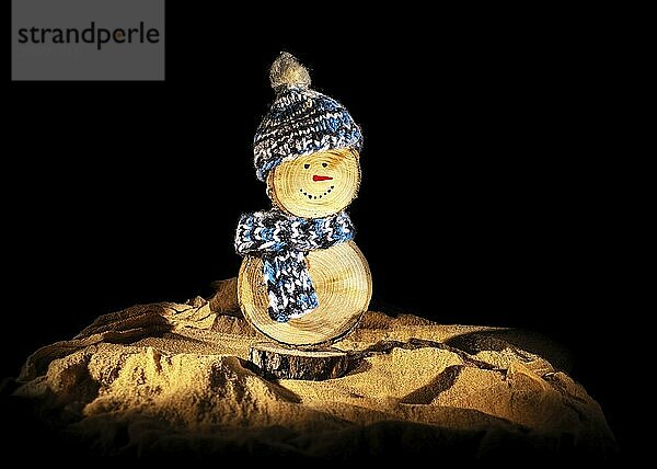 Handmade snowman made of wooden discs  with crocheted hat and scarf against a black background