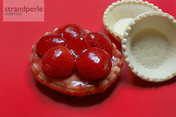 Topped strawberry tartlet and empty tartlet bases on a red background