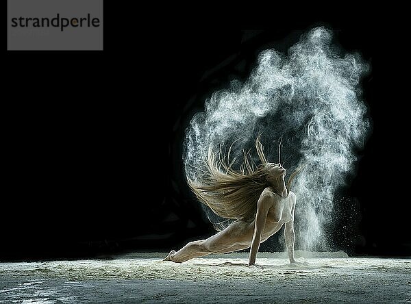 Young girl posing slenderly in a cloud of white dust in studio on black background