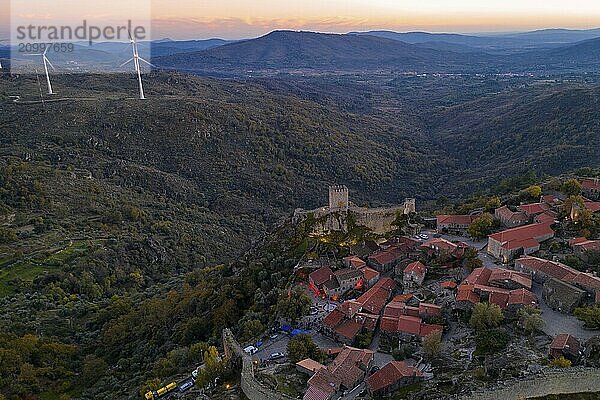 Drone aerial panorama of Sortelha historic village at sunset with lights on the castle eolic wind turbines and nature landscape  in Portugal