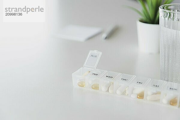 Closeup of medical pill box with doses of tablets for daily take a medicine with white  yellow drugs and capsules used for treatment  cure the disease. Glass cup of water on table  gray background