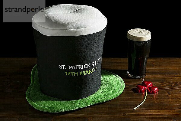 St Patrick day with a pint of black beer  hat and shamrock over a table and black background