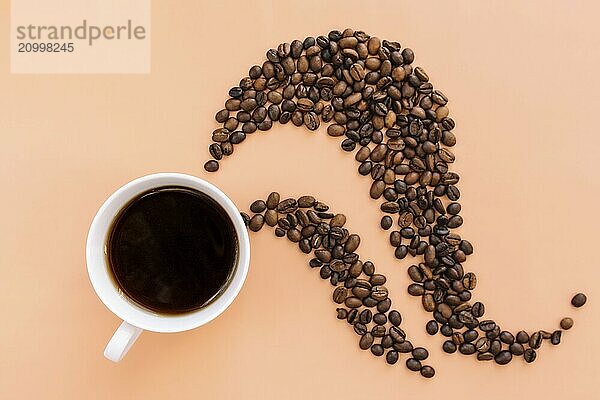 Beige flat lay background with white ceramic cup of coffee  roasted coffee beans steam shape from hot coffee. Idea and composition with coffee beans shape abstraction.