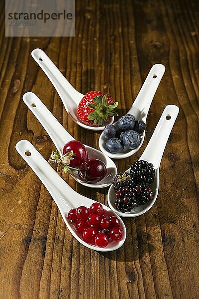 Collection of wild berries on white spoons over a wooden background