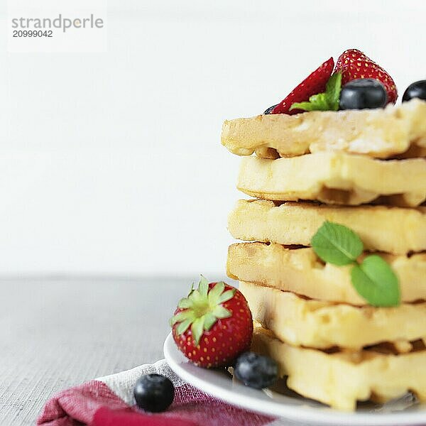 White plate on red kitchen towel with stack homemade Belgian waffles  blueberry  strawberry cuts  mint leaf  sugar powder on gray background