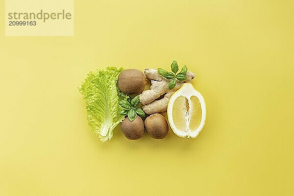 Healthy and organic food flay lay concept on yellow background. A square made of different vegetables and fruits like lemon  ginger  lettuce salad leaves  kiwi  basil