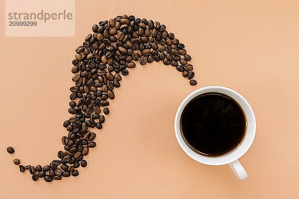 Beige flat lay background with white ceramic cup of coffee  roasted coffee beans steam shape from hot coffee. Idea and composition with coffee beans shape abstraction.