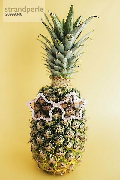 Travel and vacation concept with pineapple wearing sunglasses. Pink glasses in form of star. Relaxation on the sea. Yellow background