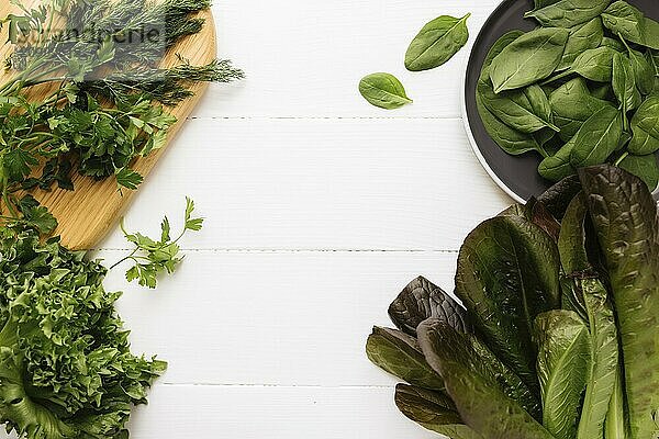 Flat lay with cutting board and bowl of fresh green salad leaves of spinach and lettuce  romaine and parsley  basil on white background. Healthy vegetarian eating concept.