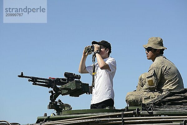 GREYMOUTH  NEW ZEALAND  NOVEMBER 18  2017: An unidentified schoolboy scans the horizon with binoculars at an open day run by the New Zealand armed forces. The machine gun is a Mag 58 GM