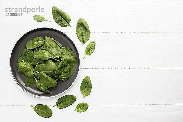 Bowl with fresh green salad leaves of spinach on a white background. Healthy vegetarian eating concept.