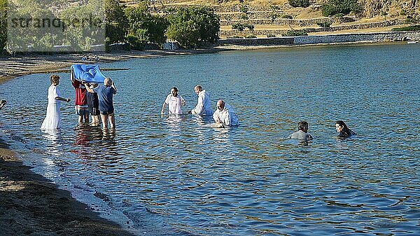 Men in white clothes and swimming costumes in the water  during a traditional ceremony on a sunny day in a hilly area  baptism in the sea  Meli beach  Patmos  Dodecanese  Greek Islands  Greece  Europe