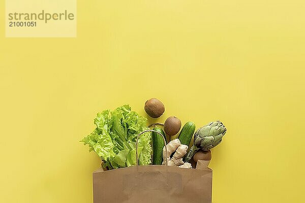 Healthy and organic food flay lay concept on yellow background. Eco bag with lettuce salad leaves  kiwi  cucumber  artichoke and ginger root