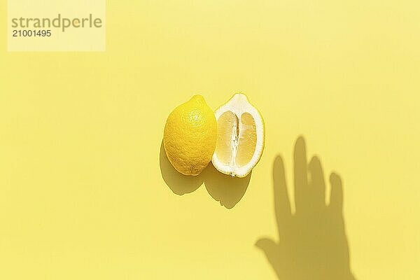 Two halved cuts of lemon with shadow from hand on yellow background. Healthy eating  travel or vacation concept