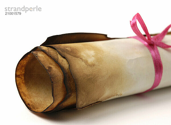 Close-up of a roll of yellowish burnt vintage parchment tied with a red ribbon Isolated over white background