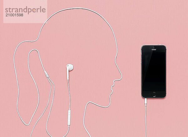 Woman head outline made by a headphone cord plugged into iPhone 5s smartphone. Music concept on pink background