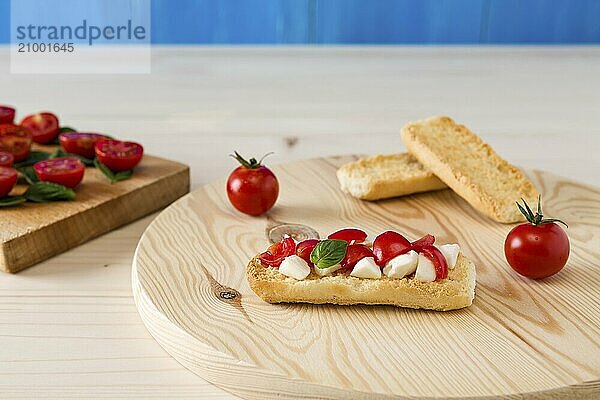 Italian crostini with mozzarella  cherry tomatoes and basil on a cutting board and blue background