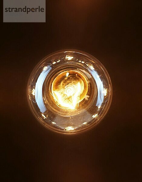 Single lit up incandescent tungsten light bulb isolated on black background