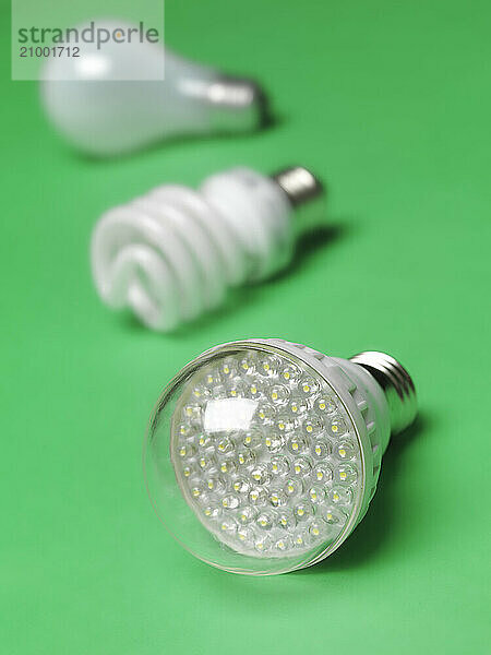 LED light bulb with fluorescent and incandescent bulbs in the background  showing three generations of light bulbs. Isolated on green