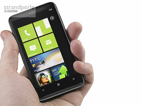 Hand with a Windows 7 phone. HTC HD7 smartphone with desktop tiles on its display isolated with clipping path on white background. High quality photo