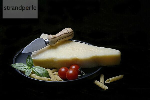 A piece of Parmesan cheese with cheese knife  pasta and tomatoes  Italy  Europe