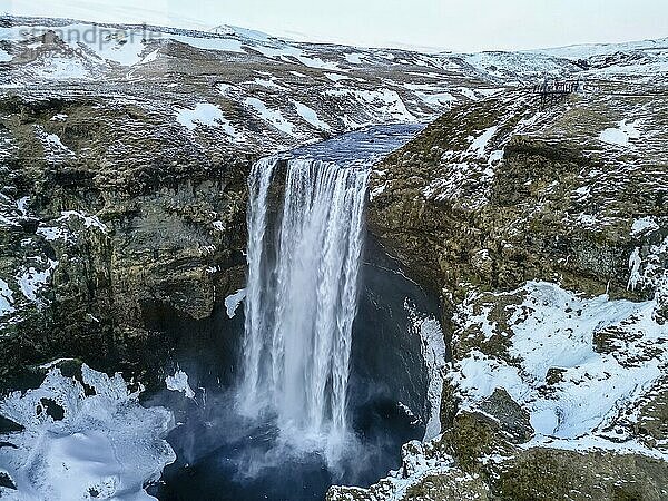 Drone aerial view of Skogafoss waterfall with snow and lots of water in winter in Iceland