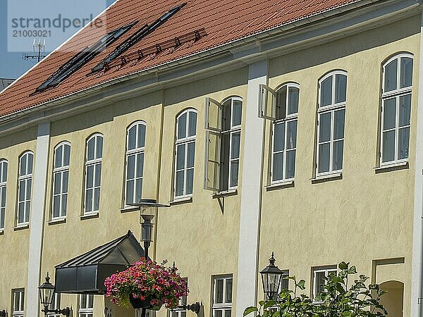 Yellow building with many windows and flower baskets under a blue sky  some windows are open  trelleborg  sweden  baltic sea  scandinavia