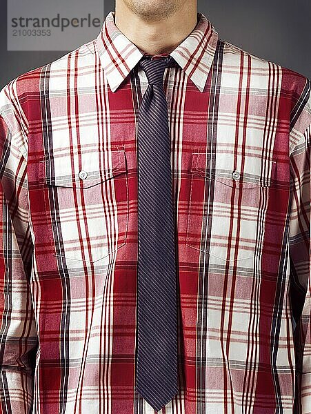 Closeup of a man wearing fancy red tartan shirt with a skinny stripy necktie on grey background