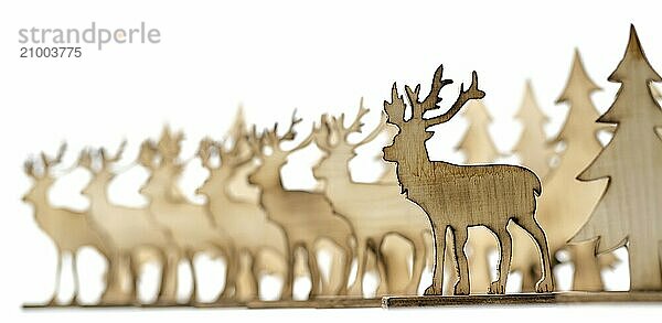 Deer figure sawn out of wood with dark edges and wooden fir trees cut out on white