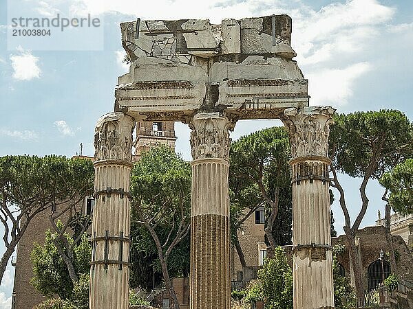 Three old columns in front of a cloudy sky and green background with trees  Rome  Italy  Europe