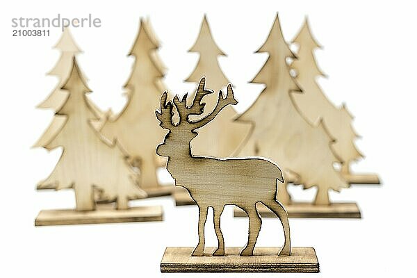 Deer figure sawn out of wood with dark edges and wooden fir trees cut out on white