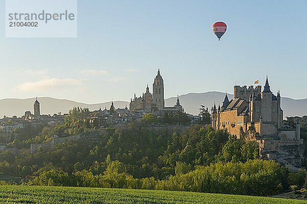 Beautiful view of a castle at sunrise with a hot air balloon in the sky and green fields in the foreground  Church  Iglesia San Esteban  Cathedral  Alcázar  Alcazar  Segovia  Castilla y León  Leon  Spain  Europe