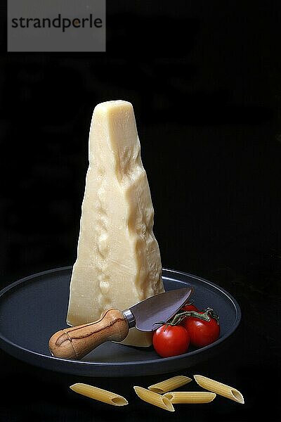 A piece of Parmesan cheese with cheese knife  pasta and tomatoes  Italy  Europe